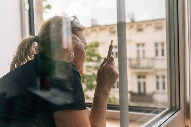 Olgun bir kadın pencerenin yanında sigara içiyor. Beyaz, 40 yaşında, kadın, sigara içiyor. Yüksek kalite fotoğraf