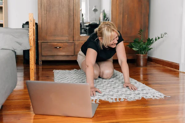 家里的成熟女人在地板上做运动瑜伽 带着笔记本电脑在网上上课 高质量的照片 — 图库照片