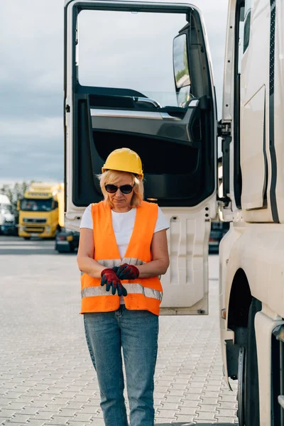 Middle age truck driver woman puts on gloves, trucker occupation in Europe for females. High quality photo