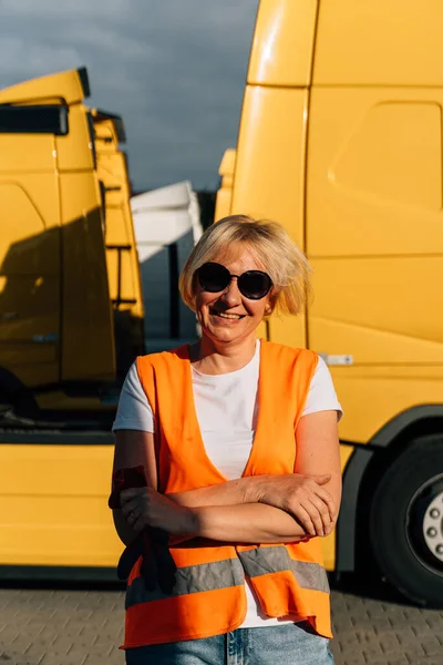 Happy middle-aged woman smiling in front of yellow semi-truck vehicle . High quality photo