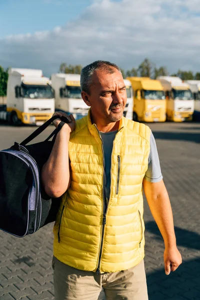 Portrait of caucasian mature man with bag on some-truck vehicles parking background. Truck driver worker . High quality photo