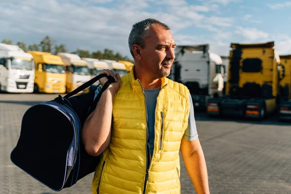 Portrait of caucasian mature man with bag on some-truck vehicles parking background. Truck driver worker . High quality photo