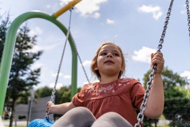 Preschooler caucasian girl swinging on rope net swing on playground . High quality photo