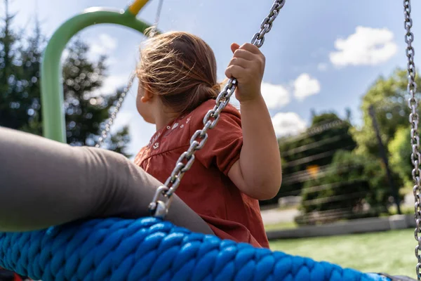 Preschooler caucasian girl swinging on rope net swing on playground . High quality photo