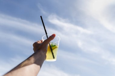 Hand with cup of lemonade on blue sky background. High quality photo