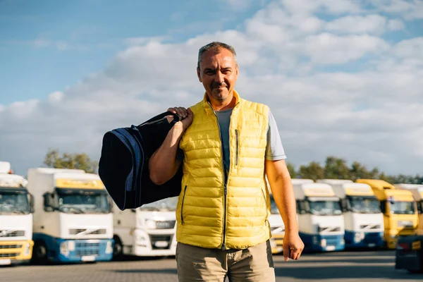 Portrait of caucasian mature man with bag on some-truck vehicles parking background. Truck driver worker . High quality photo