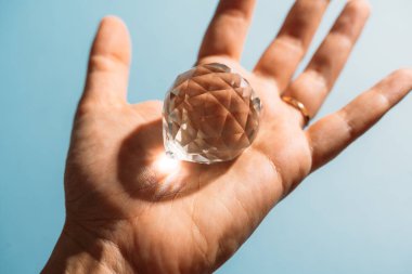 Close up hand with crystal on blue background with sun light . High quality photo