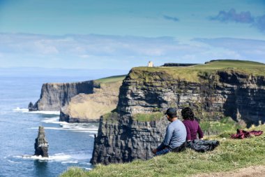 İrlanda 'nın Clare ilçesinin Burren bölgesinin güneybatı kıyısındaki Moher Uçurumları ve deniz kayalıklarına hayran olan bir çift görülüyor.