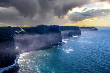 World famous cliffs of moher in county Clare Ireland with a dramatic cloudy sky with the sun rays shining through the clouds
