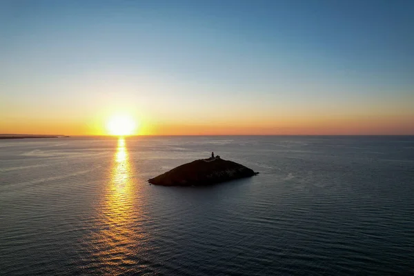 Aerial view of Ballycotton Lighthouse at sunrise from the coast of county Cork, Ireland