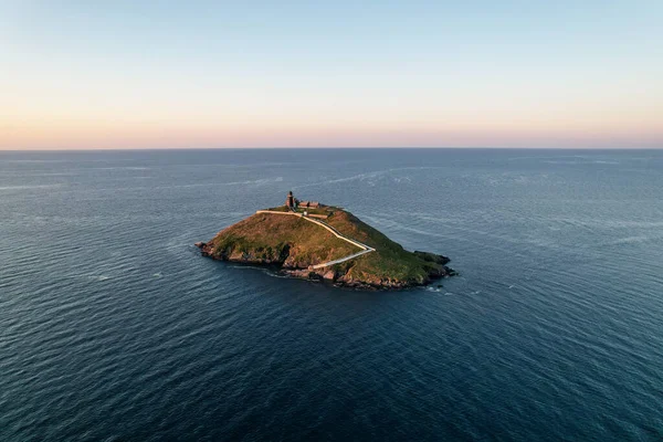 Aerial view of Ballycotton Lighthouse at sunrise from the coast of county Cork, Ireland