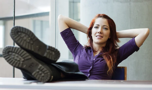 Femme d'affaires souriante, les pieds en l'air, les bras derrière la tête — Photo