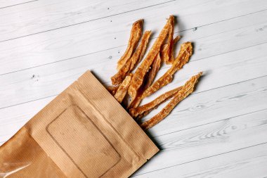 Dilimlenmiş hindi ya da tavuk eti kurutulmuş ve kahverengi kağıda sarılmış. Ev yapımı kuru köpek maması. Tahta beyaz arkaplan, logo için boş yer, kopyalama alanı.