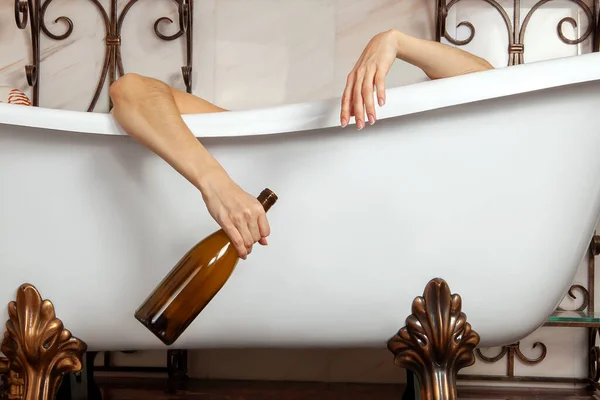 İki el antika şekilli küvette asılı, elinde epmty şarap şişesi var. Sarhoşluk, depresyon, yalnızlık, parti sonrası konsepti. Banyo ve fotokopi alanının klasik iç dekorasyonu. 