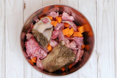 Tavuk boyunlu, etli, göbekli ve havuçlu metal evcil hayvan kasesi. Köpek konsepti için doğal organik günlük yemek hazırlığı. Boşluğu kopyala, beyaz tahta masa arkaplanı.