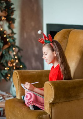 Komik beyaz kız solak Noel ağacının yanında Noel Baba 'ya mektup yazıyor. Mutlu çocukluk, mucizeler ve arzular zamanı. Mutlu Noeller..