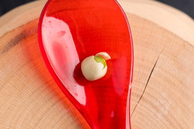 single green pea on red plastic spoon