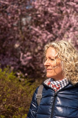 Genç kadın derin bir nefes alır ve pembe çiçeklerin önünde güneşin tadını çıkarır.