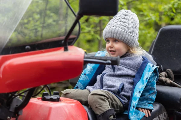 Candid portrait with selective focus on a happy four year old boy sitting slumped back in the driving seat of a quad bike. Copy space to side.