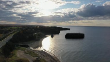 Öğleden sonra Chaleur Körfezi ve Caraquet 'deki engebeli Kanada kıyı şeridi üzerinde kayalık arazi aracı manzarası. Alçak güneş sakin denizi yansıtır..