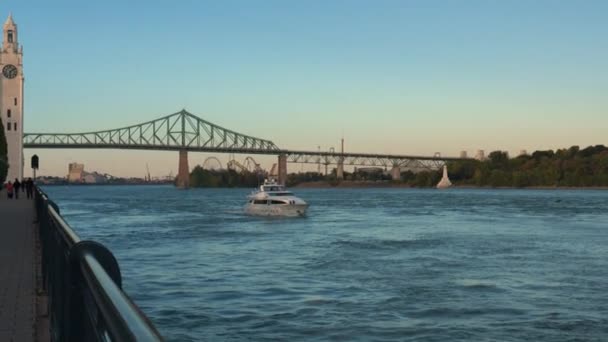 在加拿大蒙特利尔的圣劳伦斯河上看到了一艘小白色游艇 Jacques Cartier桥 蓝色天空背景下的钢桁架桥 — 图库视频影像