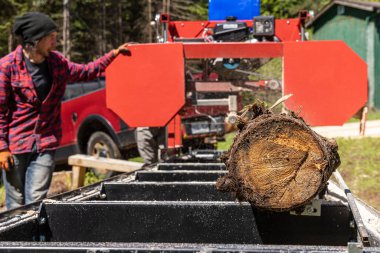 Close up selective focus shot of a blurry man at work using an industrial portable sawmill to chop a tree trunk into logs. With copy space.
