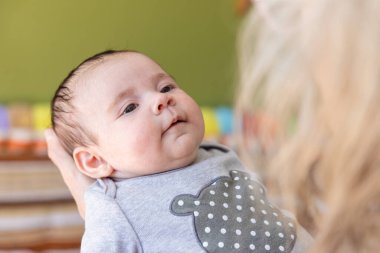 Yakın plan seçici odaklı bir bakış açısı olan yeni doğan bebek, ebeveynlerinin ya da büyükbabalarının kollarında, ön planda bulanık sarı saçlar ve yeşil arka planda.