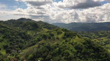 Drone footage over a small farming community by rugged hilly terrain in the Philippines. Rooftops of small buildings dotted around side of mountain.
