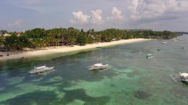 Panoramic aerial views of beachfront holiday resorts and traditional boats moored in the shallow seafront with palm trees and white sandy beach.