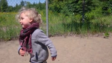 An adorable two year old boy is seen from the side in slow motion, running towards mother and newborn child on swings in a recreational playground.