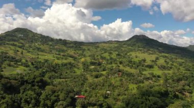 Filipinler 'in kırsal kesimlerinde mavi gökyüzü ve dağınık bulutlarla yeşil tepelerin ve dağların üzerinden geçen kamera görüntüleri..