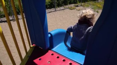 Mavi oyun parkının tepesinden yavaş çekim görüntüsü. Üç yaşındaki mutlu bir çocuk otururken ve dipteki kumlu zemine kayarken. Kopyalama alanı ile.
