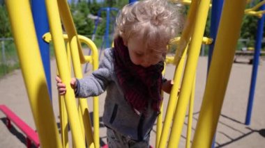 Close up front video in slow mo, as inquisitive three year old caucasian boy is seen exploring the climbing frame and kids apparatus at local park.