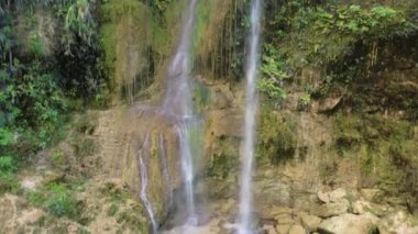 Filipinler 'deki yemyeşil bir ormandaki sığ bir dereden akan, doğal segmentli bir şelalenin dibinden tepesine uçan insansız hava aracı görüntüleri..
