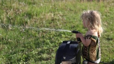 Closeup side view in slow motion as two year old boy is having fun with the garden hose, spraying and wasting a lot of water around on the grass