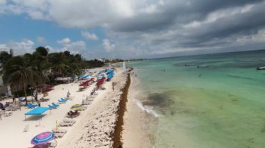 Aerial video above a popular beach in Playa del Carmen, Mexico. With tourists enjoying tropical climate and colorful parasols and sun loungers.