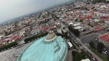 Camera panning over the turquoise roof of the modern basilica, crowned with stone cross at the Basilica of Our Lady of Guadalupe in Mexico City.