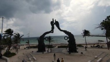 21. yüzyıl Portal Maya sanat heykelinin altında, palmiye ağaçları ve turistlerle birlikte Playa del Carmen plajında alçaktan uçan bir dron..