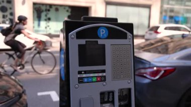 Closeup selective focus clip on a car parking meter on a street in central Montreal, a blurry cyclist is seen riding by in background with copy space.