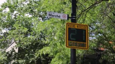 Closeup footage of a radar speed sign working on a street in Montreal, Canada. Numerical display showing speed of passing traffic against green trees.