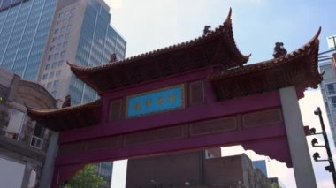 Short clip of the traditional Asian architecture of a red paifang arched gateway in Chinatown, Montreal with modern high rise buildings in background.