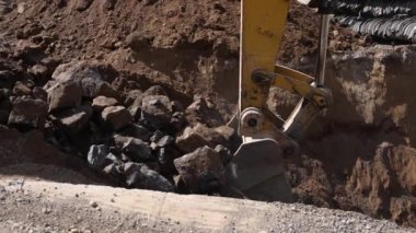 Close up video with side profile view on the hydraulic boom, with moving piston and bucket scooping up dirt and rubble from a deep hole in ground.