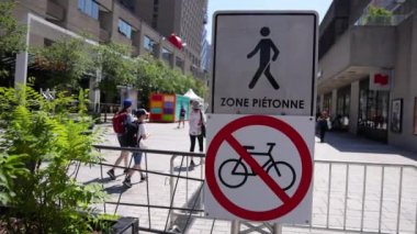 Close up slow motion footage of a no cycling sign on a pedestrianized street in central Montreal, Canada. Blurry people walk by in background.