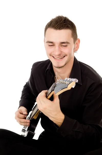 Молодой парень в черной одежде сидит и играет на гитаре — стоковое фото
