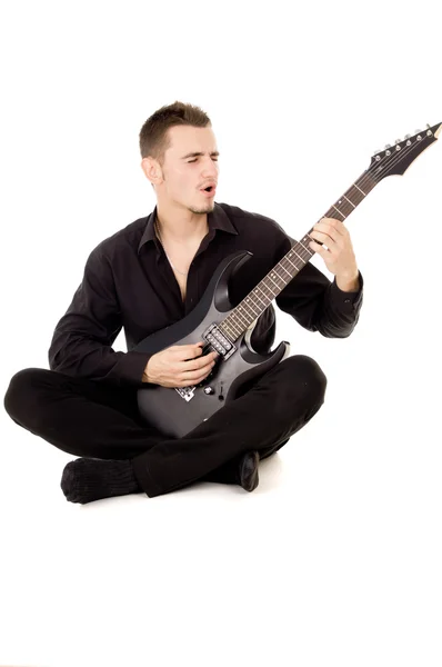 黒い服に身を包んだ若い男に座っているし、ギターを弾く — ストック写真