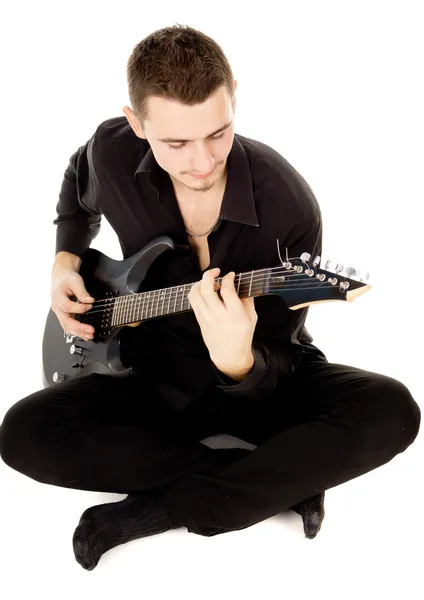 Young man dressed in black clothes sits and plays the guitar — Stock Photo, Image