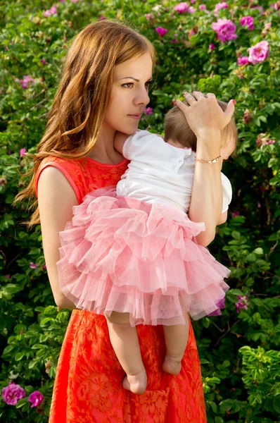 Mãe feliz segurando um bebê em um fundo de flores — Fotografia de Stock