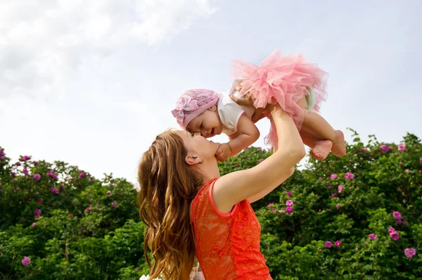 Glad mamma håller ett barn på en bakgrund av blommor — Stockfoto