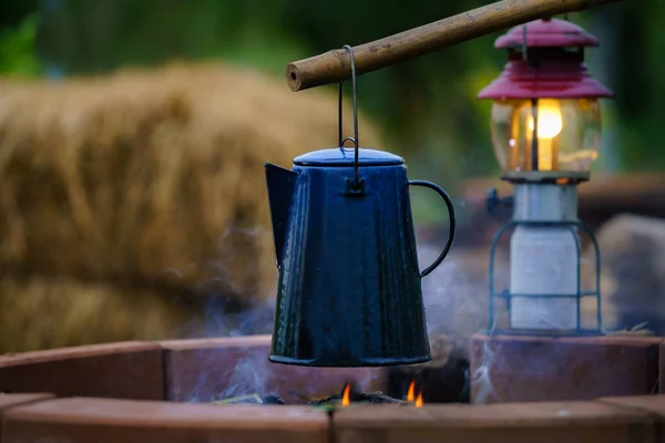 搪瓷咖啡杯 葡萄酒水壶在夜间露营时着火 背景是一个古老的煤气灯 软聚焦 浅聚焦效应 — 图库照片