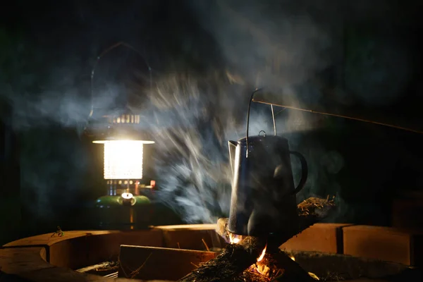 搪瓷咖啡杯 葡萄酒水壶在夜间露营时着火 背景是一个古老的煤气灯 软聚焦 浅聚焦效应 — 图库照片
